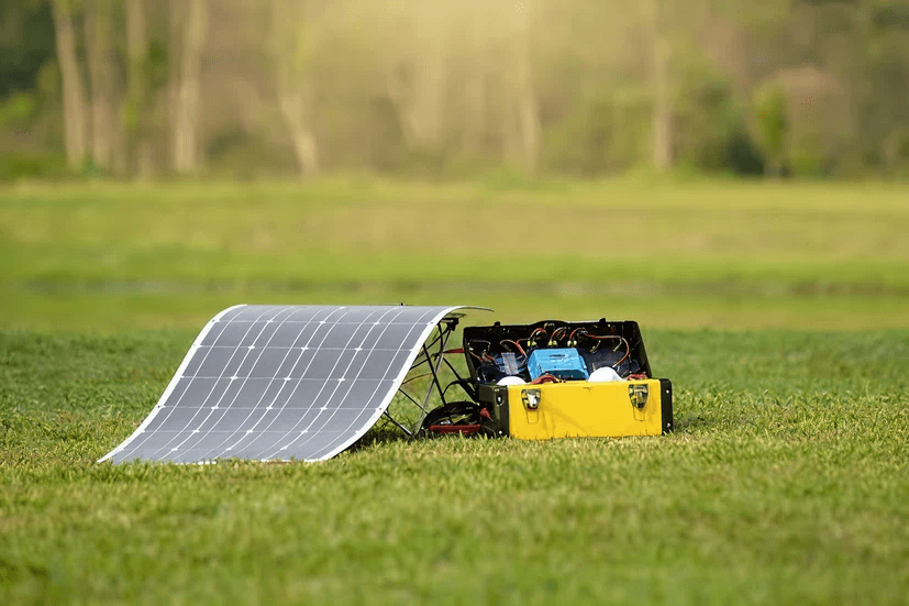 Panneau solaire souple Heliup déroulé sur l'herbe et relié à une batterie portable